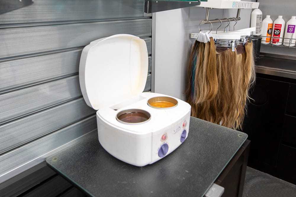 Wax warmer open on salon table with hair extensions and hair products nearby.