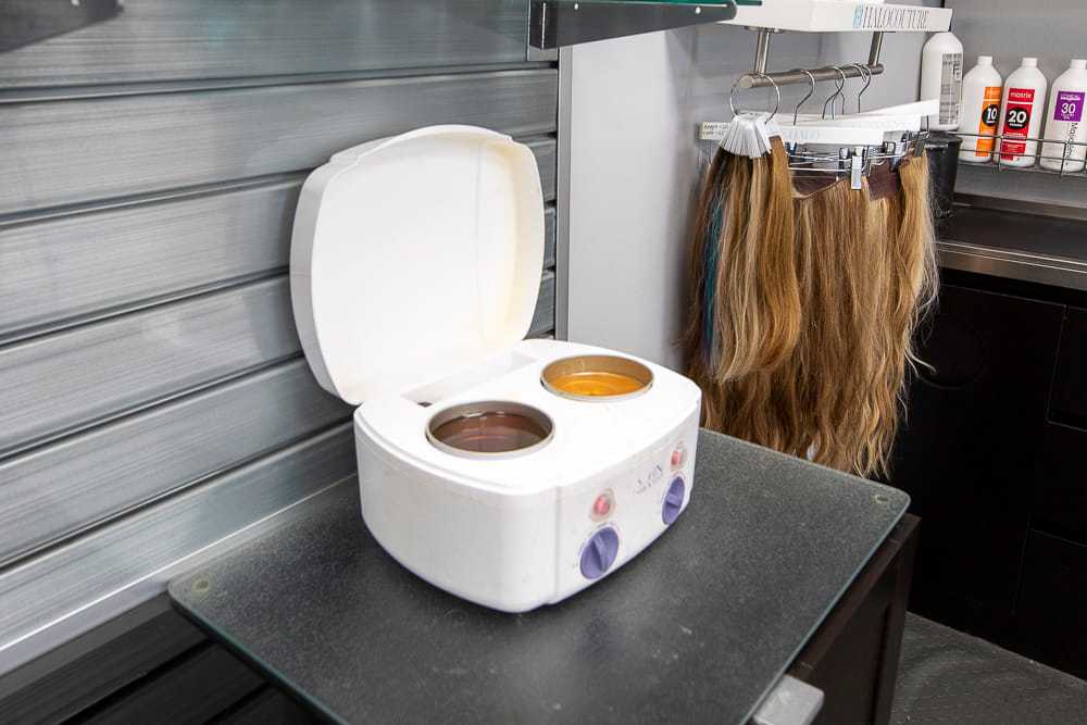 Wax warmer open on salon table with hair extensions and hair products nearby.