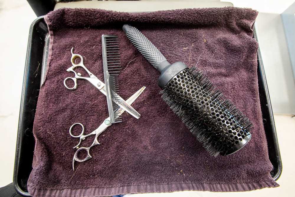Hair styling tools: scissors, comb, and round brush on a dark towel.