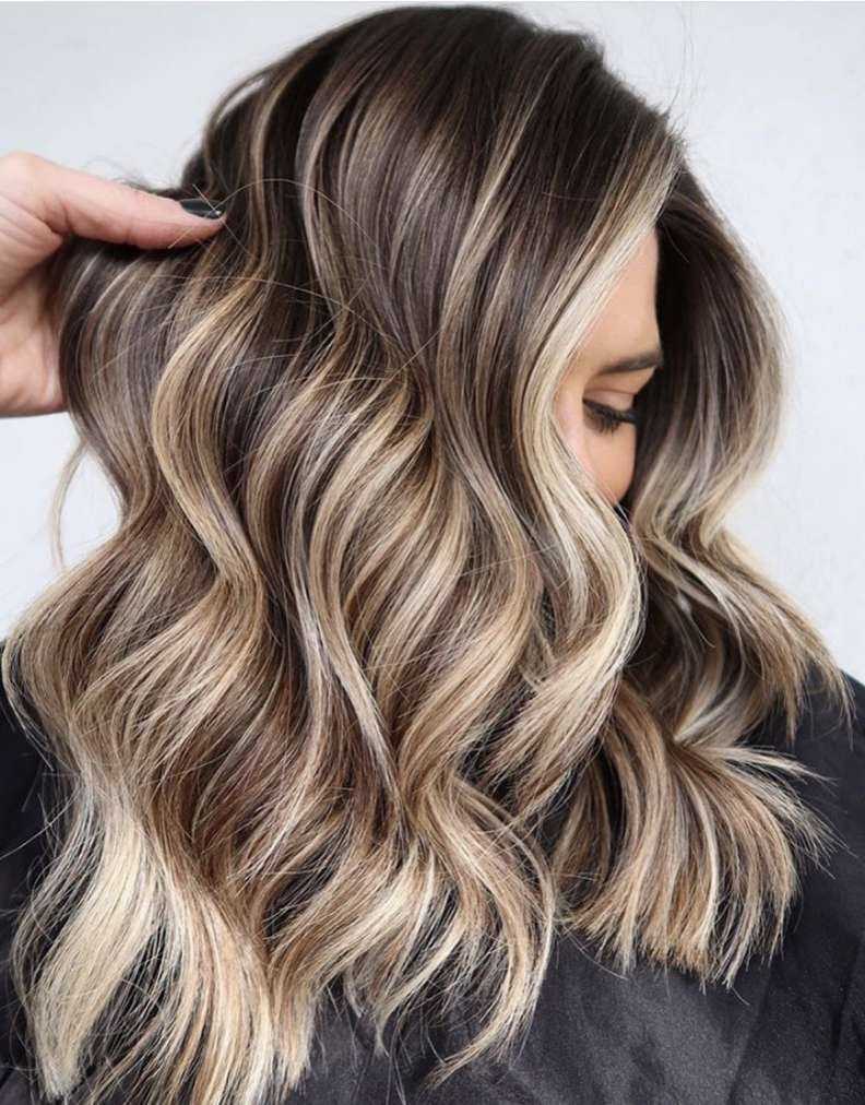 Wavy brunette hair with blonde highlights styled in loose waves.